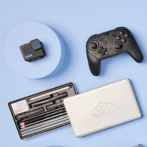 A gaming controller, a small camera, and art supplies arranged on a light blue background.