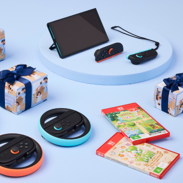 A gaming console with controllers, a carrying strap, two wrapped gifts with blue ribbons, and video game cases on a light blue circular surface.